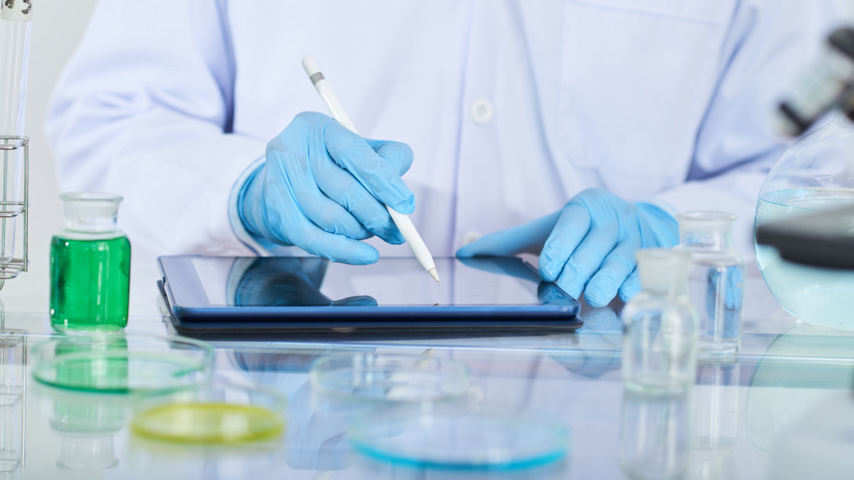 Científico con matraces y tableta digital.